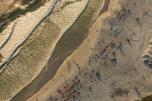 Aerial view of a sandy beach with colorful umbrellas people walking and relaxing on the sand and gentle waves rolling onto the shore in Rio de Janeiro Rio de Janeiro Brazil. Aerial view of a sandy beach with colorful umbrellas people walking and relaxing on the sand and gentle waves rolling onto the shore in Rio de Janeiro Rio de Janeiro Brazil.