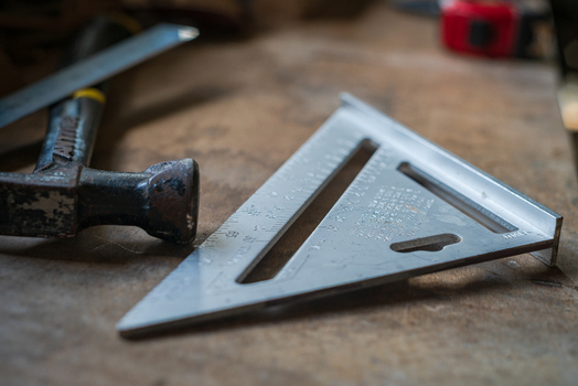 View of a metal speed square and a claw hammer resting on a wooden workbench in a workshop in Looe Cornwall United Kingdom. View of a metal speed square and a claw hammer resting on a wooden workbench in a workshop in Looe Cornwall United Kingdom.