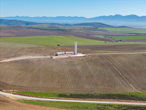 Aerial view of a wind turbine under construction with blades on the ground amidst rolling agricultural fields and distant mountains in Swellendam Western Cape South Africa. Aerial view of a wind turbine under construction with blades on the ground amidst rolling agricultural fields and distant mountains in Swellendam Western Cape South Africa.
