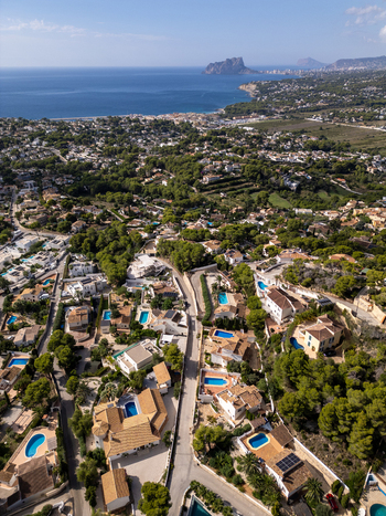 Aerial view of residential villas with swimming pools and lush pine trees in the coastal town of Moraira Valencian Community Spain.