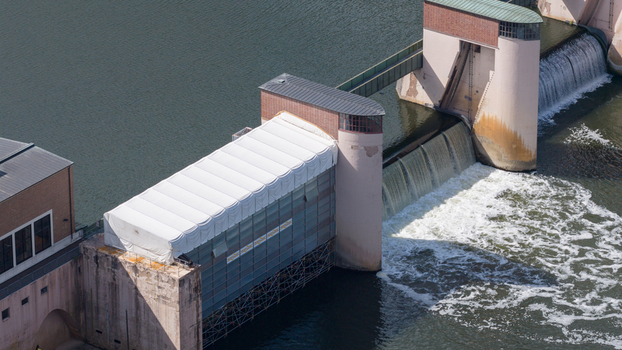 Aerial view of the Rockenau lock and weir on the Neckar River featuring concrete structures and a white tent covered section in Eberbach Baden Wurttemberg Germany.
