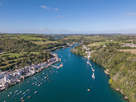 Aerial view of the Fowey river flowing past the historic town of Fowey with boats moored in the water and lush green hills in the background Fowey Cornwall United Kingdom. Aerial view of the Fowey river flowing past the historic town of Fowey with boats moored in the water and lush green hills in the background Fowey Cornwall United Kingdom.