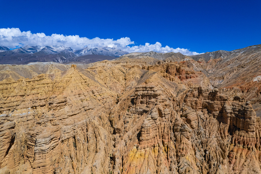Aerial view of rugged layered golden brown rock formations and deep canyons in the arid landscape of the Himalayas in Nepal.