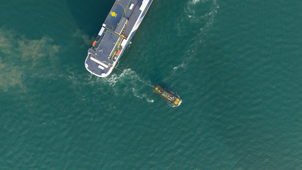 Aerial view of a large cargo ship being assisted by a tugboat in the turquoise waters of the port area in Laem Chabang Chon Buri Thailand.