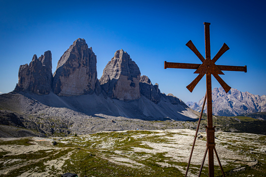 View of the Tre Cime di Lavaredo mountain peaks with a weathered metal cross in the foreground under a clear blue sky in Auronzo di Cadore Veneto Italy.