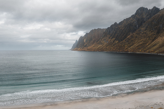 Aerial view of the dramatic coastline and sandy beach of Senja island with rugged mountains under a cloudy sky in Senja Troms Norway.