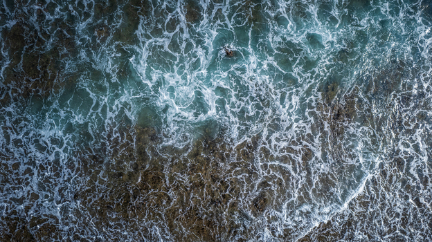 Aerial view of ocean waves crashing over a rocky reef shoreline with turquoise water and white sea foam in Bajawa Nusa Tenggara Timur Indonesia. Aerial view of ocean waves crashing over a rocky reef shoreline with turquoise water and white sea foam in Bajawa Nusa Tenggara Timur Indonesia.