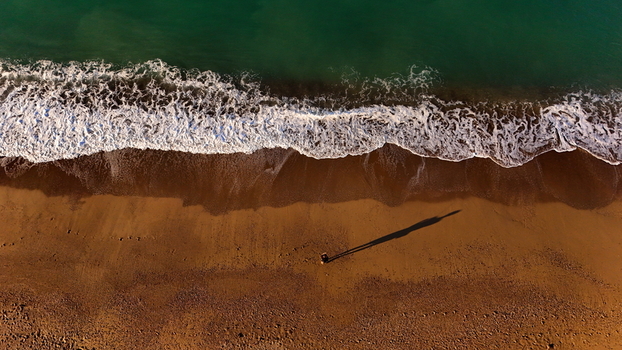 Aerial view of Manavgat Mendirek showing the sandy beach with gentle waves washing ashore and a person standing on the sand casting a long shadow in Manavgat Antalya Turkiye.