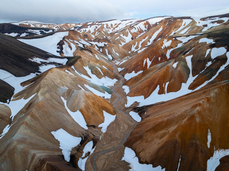 Aerial view of Landmannalaugar featuring colorful rhyolite mountains with patches of snow and a winding riverbed in Rangarthing ytra Iceland. Aerial view of Landmannalaugar featuring colorful rhyolite mountains with patches of snow and a winding riverbed in Rangarthing ytra Iceland.