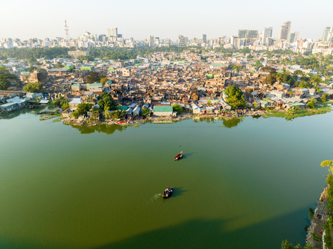 Aerial view of boats gently glide on the tranquil lake contrasting with the densely packed houses of the Dhaka slums and distant skyline Dhaka Dhaka Division Bangladesh. Aerial view of boats gently glide on the tranquil lake contrasting with the densely packed houses of the Dhaka slums and distant skyline Dhaka Dhaka Division Bangladesh.