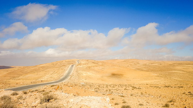 View of the asphalt road winding through the arid landscape of the Wadi Rum Desert under a bright blue sky with scattered clouds in Wadi Rum Village Aqaba Governorate Jordan. View of the asphalt road winding through the arid landscape of the Wadi Rum Desert under a bright blue sky with scattered clouds in Wadi Rum Village Aqaba Governorate Jordan.