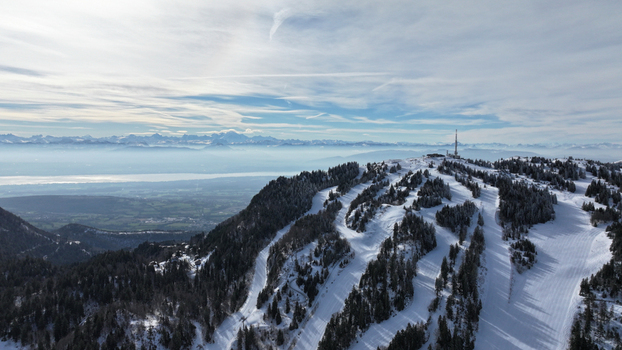 Aerial view of a snow covered mountain with ski tracks under a bright sky silhouetted against distant peaks and valleys Gex Auvergne Rhône Alpes France. Aerial view of a snow covered mountain with ski tracks under a bright sky silhouetted against distant peaks and valleys Gex Auvergne Rhône Alpes France.