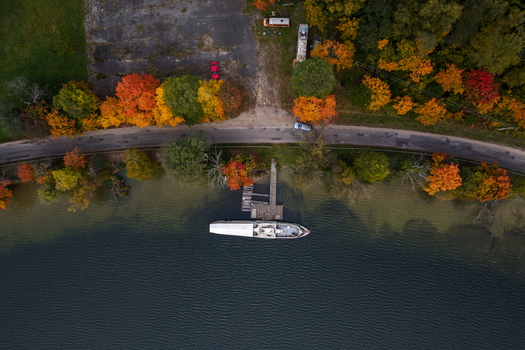 Aerial view of a boat docked at a wooden pier along a lake shore lined with vibrant autumn trees and a winding road in Trakai Vilnius County Lithuania. Aerial view of a boat docked at a wooden pier along a lake shore lined with vibrant autumn trees and a winding road in Trakai Vilnius County Lithuania.