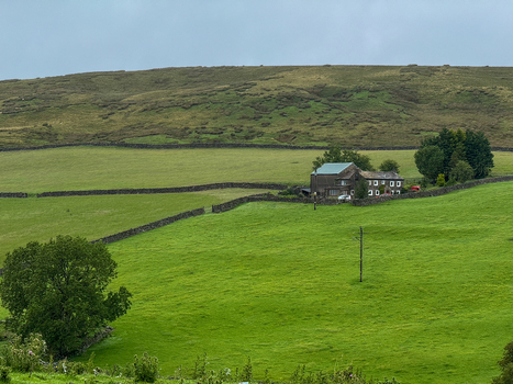 View of a traditional stone farmhouse nestled among green pastures and dry stone walls in the rolling hills of Yorkshire in Hawes England United Kingdom. View of a traditional stone farmhouse nestled among green pastures and dry stone walls in the rolling hills of Yorkshire in Hawes England United Kingdom.