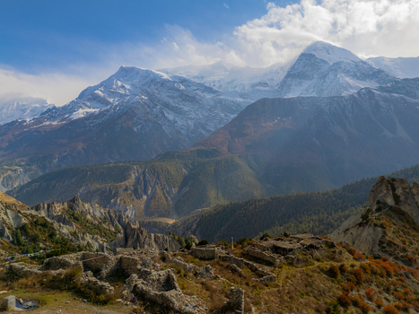 Aerial view of ancient stone ruins nestled in the Himalayan mountains featuring snow capped peaks rugged terrain and sparse autumn vegetation Nepal.