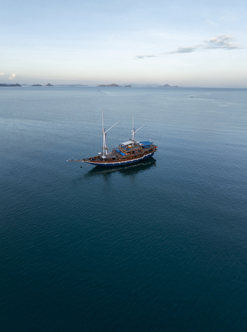 Aerial view of a traditional wooden Phinisi boat sailing on the calm blue waters near the Labuan Bajo coastline Komodo East Nusa Tenggara Indonesia. Aerial view of a traditional wooden Phinisi boat sailing on the calm blue waters near the Labuan Bajo coastline Komodo East Nusa Tenggara Indonesia.