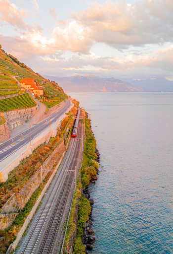 Aerial view of a train traveling along the tracks beside the terraced vineyards of Lavaux and the shores of Lake Geneva at sunset in Bourg en Lavaux Vaud Switzerland. Aerial view of a train traveling along the tracks beside the terraced vineyards of Lavaux and the shores of Lake Geneva at sunset in Bourg en Lavaux Vaud Switzerland.