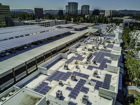 Aerial view of solar panel infrastructure installed on a large parking structure roof with urban buildings in the background in San Fernando California United States. Aerial view of solar panel infrastructure installed on a large parking structure roof with urban buildings in the background in San Fernando California United States.