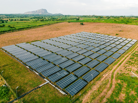 Aerial view of a large solar panel farm situated in a rural landscape with green fields and a rocky hill in the background in Ogun State Nigeria.