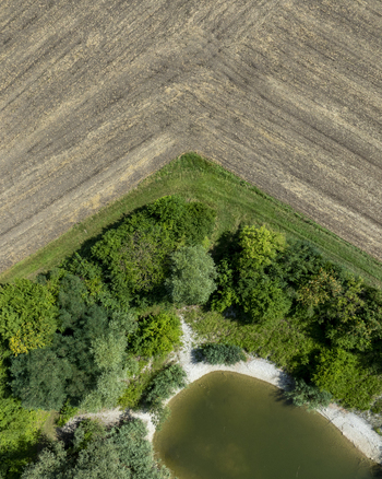 Aerial view of a small pond surrounded by lush green trees and adjacent to harvested agricultural fields in Aschheim Bavaria Germany.