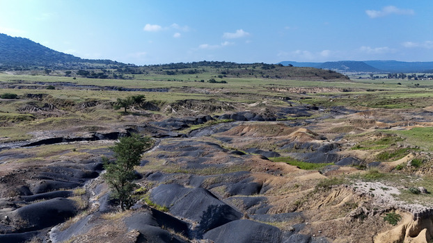 Aerial view of eroded dark soil mounds and green fields with sparse trees under a clear blue sky in the rural landscape of Pietermaritzburg KwaZulu Natal South Africa.