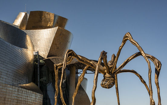 View of the Guggenheim Museum Bilbao and the Maman spider sculpture with shimmering titanium panels under a clear blue sky in Bilbao Euskadi Spain. View of the Guggenheim Museum Bilbao and the Maman spider sculpture with shimmering titanium panels under a clear blue sky in Bilbao Euskadi Spain.