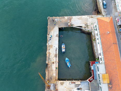 Aerial view of Ginjal Pier with small blue boats moored in the basin and fishermen on the concrete dock Almada Setubal Portugal. Aerial view of Ginjal Pier with small blue boats moored in the basin and fishermen on the concrete dock Almada Setubal Portugal.