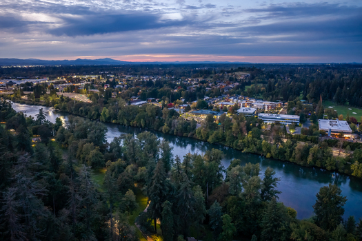 Aerial view of the Willamette River winding past Downtown Riverfront Park and illuminated neighborhoods at twilight in Eugene Oregon United States. Aerial view of the Willamette River winding past Downtown Riverfront Park and illuminated neighborhoods at twilight in Eugene Oregon United States.