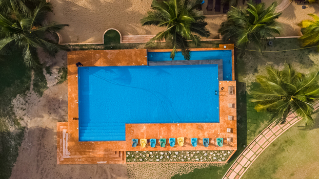 Axim Western Region Ghana 09 February 2023 Aerial view of Lou Moon Resort featuring a vibrant blue swimming pool surrounded by a terracotta deck palm trees and sandy grounds. Axim Western Region Ghana 09 February 2023 Aerial view of Lou Moon Resort featuring a vibrant blue swimming pool surrounded by a terracotta deck palm trees and sandy grounds.