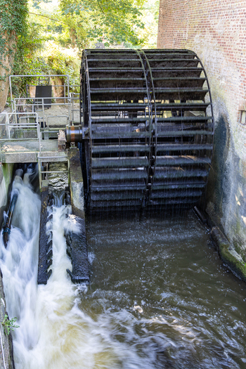View of a large historic water wheel rotating with rushing water next to a traditional brick wall and green foliage in Ribe Denmark. View of a large historic water wheel rotating with rushing water next to a traditional brick wall and green foliage in Ribe Denmark.