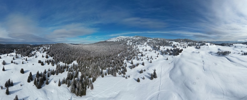 Aerial view of a snow laden landscape with forests and a distant mountain peak under a bright sky Mijoux Auvergne Rhône Alpes France. Aerial view of a snow laden landscape with forests and a distant mountain peak under a bright sky Mijoux Auvergne Rhône Alpes France.