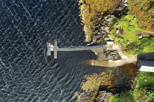 Aerial view of the wooden pier at Dunvegan Castle and Gardens extending into the dark coastal waters with rugged rocks and green grassy banks Isle of Skye Scotland United Kingdom. Aerial view of the wooden pier at Dunvegan Castle and Gardens extending into the dark coastal waters with rugged rocks and green grassy banks Isle of Skye Scotland United Kingdom.