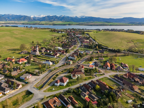 Aerial view of the village of Liptovsky Trnovec with red roofed houses a church and the Liptovska Mara reservoir against snowy mountains in Liptovsky Trnovec Zilina Region Slovakia.