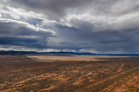 Aerial view of the vast arid outback landscape with red soil and sparse vegetation under dramatic storm clouds in Flinders Ranges South Australia Australia.