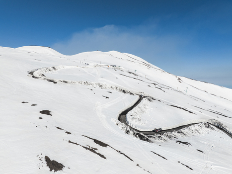 Aerial view of the Mount Etna south slope with a winding asphalt road carved through deep snow under a clear blue sky Nicolosi Sicilia Italy. Aerial view of the Mount Etna south slope with a winding asphalt road carved through deep snow under a clear blue sky Nicolosi Sicilia Italy.