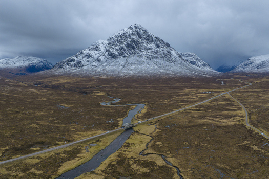 Aerial view of River Etive Bridge crossing the winding river with the snow capped Buachaille Etive Mor mountain under a moody sky Ballachulish Scotland United Kingdom. Aerial view of River Etive Bridge crossing the winding river with the snow capped Buachaille Etive Mor mountain under a moody sky Ballachulish Scotland United Kingdom.