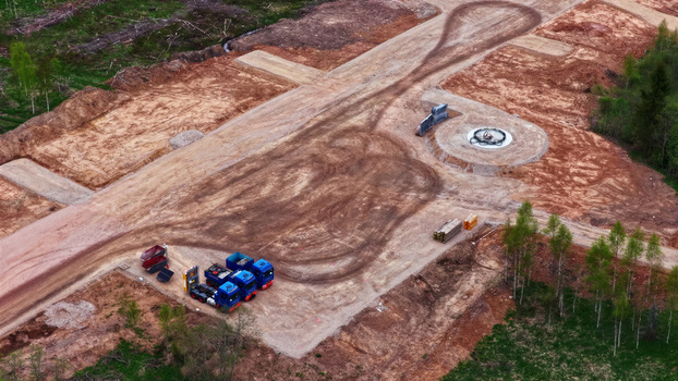Aerial view of wind turbine base construction site with a concrete foundation heavy trucks parked nearby and cleared earth in a rural landscape Latvija. Aerial view of wind turbine base construction site with a concrete foundation heavy trucks parked nearby and cleared earth in a rural landscape Latvija.