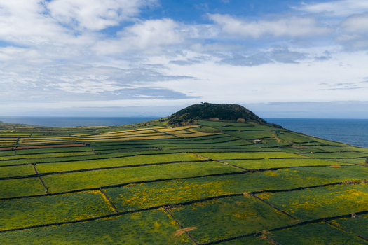 Aerial view of Terceira Island with green agricultural fields divided by stone walls and a volcanic hill overlooking the ocean Azores Portugal. Aerial view of Terceira Island with green agricultural fields divided by stone walls and a volcanic hill overlooking the ocean Azores Portugal.