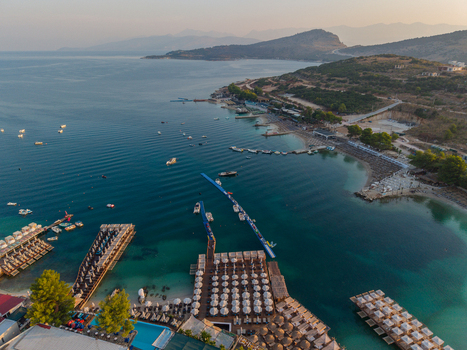 Aerial view of the turquoise waters and sandy beaches of Ksamil with rows of sun loungers wooden piers and small boats along the coastline in Ksamil Vlore County Albania. Aerial view of the turquoise waters and sandy beaches of Ksamil with rows of sun loungers wooden piers and small boats along the coastline in Ksamil Vlore County Albania.