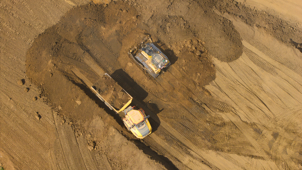 Aerial view of Black Cat Roundabout showing heavy machinery groundworks with a bulldozer and a dump truck moving earth at a construction site in Chawston England United Kingdom. Aerial view of Black Cat Roundabout showing heavy machinery groundworks with a bulldozer and a dump truck moving earth at a construction site in Chawston England United Kingdom.