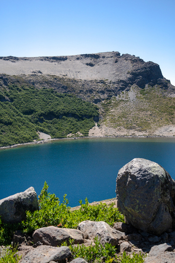 View of the crater lake at Volcan Batea Mahuida with rocky slopes and green vegetation under a clear blue sky in Alumine Neuquen Argentina. View of the crater lake at Volcan Batea Mahuida with rocky slopes and green vegetation under a clear blue sky in Alumine Neuquen Argentina.