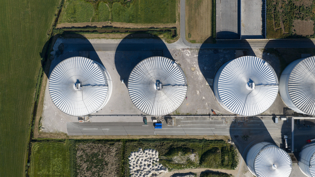 Aerial view of the Cosun Beet Company facility featuring large circular storage silos with metallic roofs long shadows and surrounding fields in Groningen Groningen Netherlands. Aerial view of the Cosun Beet Company facility featuring large circular storage silos with metallic roofs long shadows and surrounding fields in Groningen Groningen Netherlands.