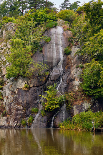 Ronneby Blekinge County Sweden 11 September 2025 View of a small waterfall cascading down a dark mossy rock face surrounded by lush green trees in Brunssparken. Ronneby Blekinge County Sweden 11 September 2025 View of a small waterfall cascading down a dark mossy rock face surrounded by lush green trees in Brunssparken.
