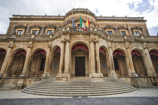 View of the historic Palazzo Ducezio with its elegant Baroque facade and arched portico under a cloudy sky in Noto Sicily Italy. View of the historic Palazzo Ducezio with its elegant Baroque facade and arched portico under a cloudy sky in Noto Sicily Italy.