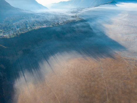 Aerial view of Cemorolawang village on the edge of a volcanic caldera with morning mist and dramatic shadows across the arid landscape in Kecamatan Sukapura Jawa Timur Indonesia.
