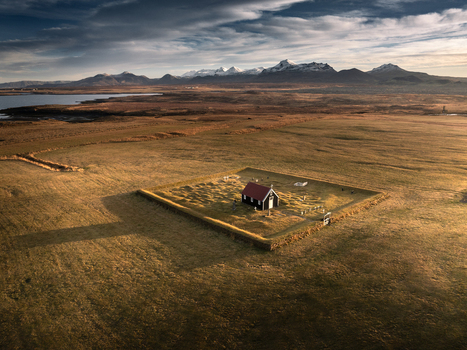 Aerial view of the historic Budakirkja black church surrounded by a square stone wall and vast fields with snow capped mountains in the distance Iceland.