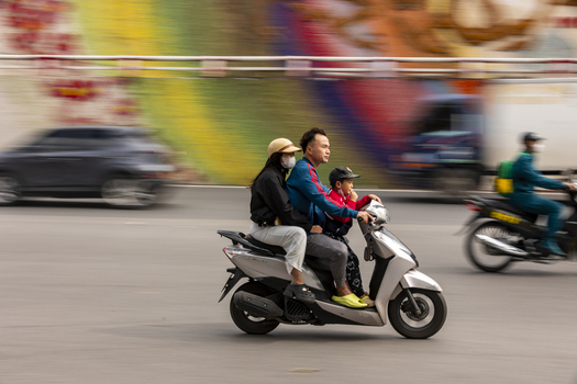 Hanoi Ha Noi Vietnam 11 November 2025 View of a family of three riding a scooter through a busy street in Hanoi with a colorful mural in the background.