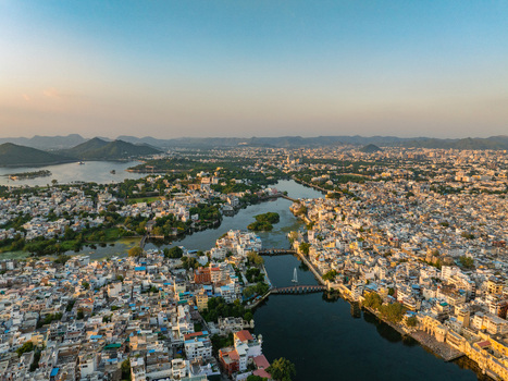 Aerial view of the historic city of Udaipur with its dense urban architecture interconnected lakes and distant hills under the soft light of the golden hour in Udaipur Rajasthan India.