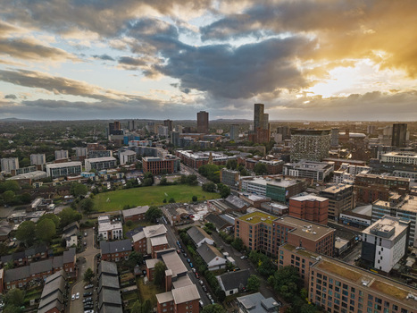 Aerial view of the Birmingham city skyline at sunset featuring modern and historic buildings dense urban rooftops and green spaces in Birmingham England United Kingdom.