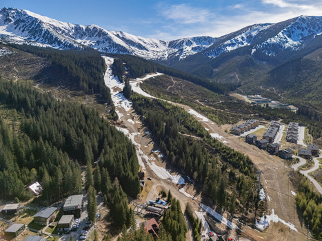 Aerial view of the Jasna ski resort area with melting snow on slopes dense pine forests and chalets nestled in the valley under the Low Tatras peaks in Demanovska Dolina Zilina Region Slovakia.